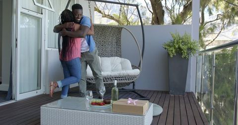 Joyful couple embracing on sunlit patio with drinks
