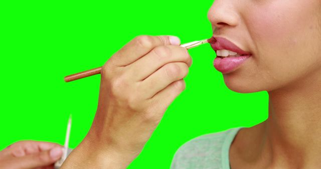 Make up artist putting lip gloss on models face on green screen background