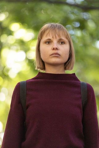 Young woman standing and looking upward in sunlit park wearing maroon sweater and backpack