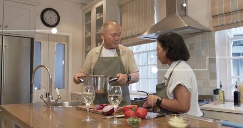 Mature couple cooking together at kitchen island, chopping vegetables and sharing wine