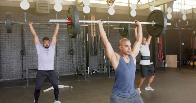 Focused biracial sports people exercising and lifting weight bars at gym. Activity, sport, togetherness and exercise, unaltered.