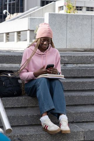 African american student studying on urban campus steps using smartphone and notebook