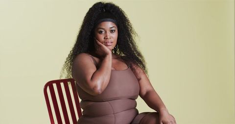 Confident African American Woman in Brown Bodysuit on Red Chair