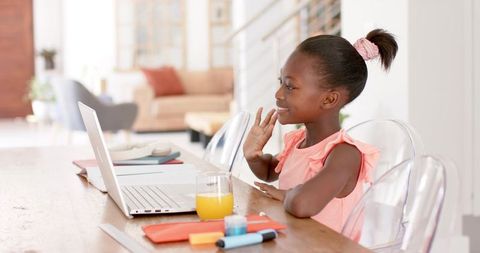 African girl waving during remote learning at home with laptop and orange juice