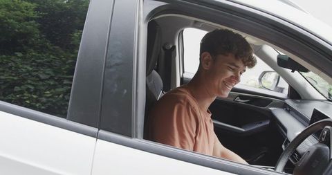 Young man smiling while sitting in driver seat of modern white car, candid happy commuter