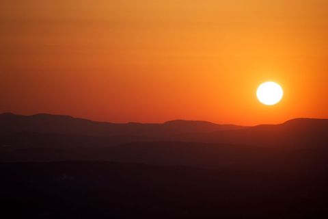Golden Sunset Over Layered Mountain Silhouettes With Warm Orange Sky and Sun Near Horizon