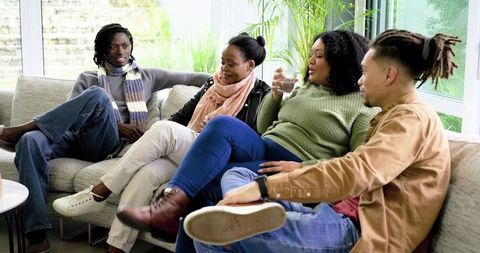 African American Friends Relaxing and Chatting on Sofa in Bright Sunroom