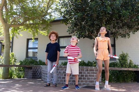 Diverse children standing holding rolled certificates outside school celebrating success