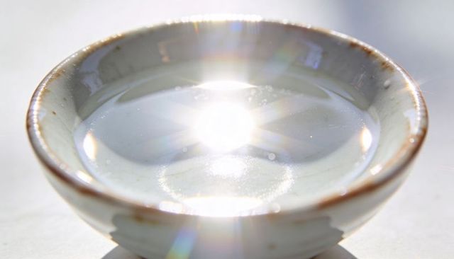 Sunlit ceramic bowl reflecting bright starburst over water with lens flare and bokeh