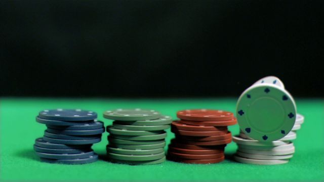 Close-up of poker chips stacked on green table with falling white chip in slow motion against black background. Ideal for use in casinos, gambling-themed projects, online betting sites, and advertisements related to poker games.