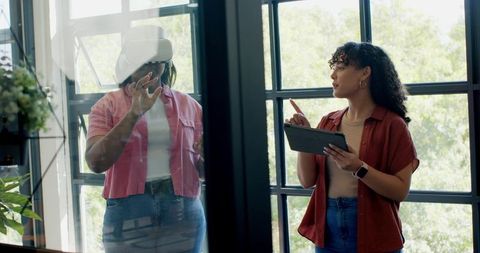 Diverse female coworkers collaborating with vr headset and tablet in modern glass office
