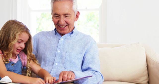 Smiling Grandpa Reading Storybook with Granddaughter on Sofa - Download Free Stock Images Pikwizard.com