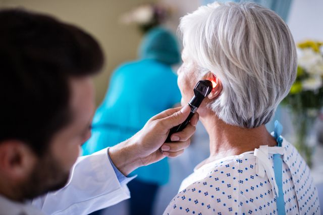 Doctor using otoscope to examine senior woman's ear in medical clinic. Ideal for content on healthcare, senior wellness, medical checkups, ear examinations, and doctor-patient interactions.