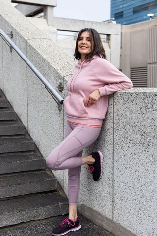 Middle-aged woman leaning on concrete wall by stairway wearing pastel activewear smiling