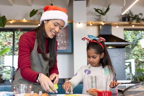 Asian mother and daughter baking christmas cookies together in cozy sunlit kitchen