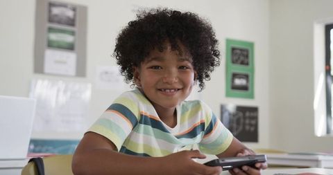 African american boy smiling while holding handheld game controller in classroom