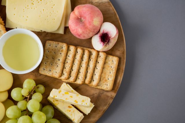 Variety of cheese with grapes, peach and crackers on wooden plate