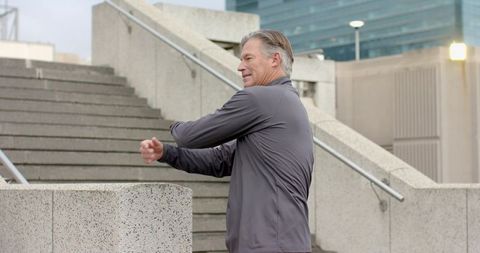 Mature man stretching and twisting on urban concrete steps during outdoor workout