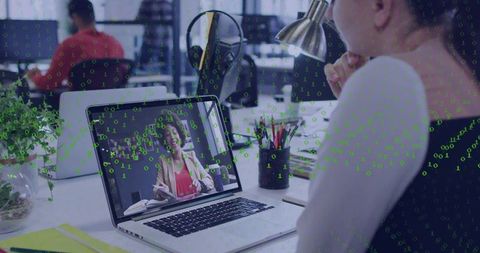 Woman Viewing Virtual Meeting on Laptop in Open-Plan Office with Green Binary Cyber Overlay