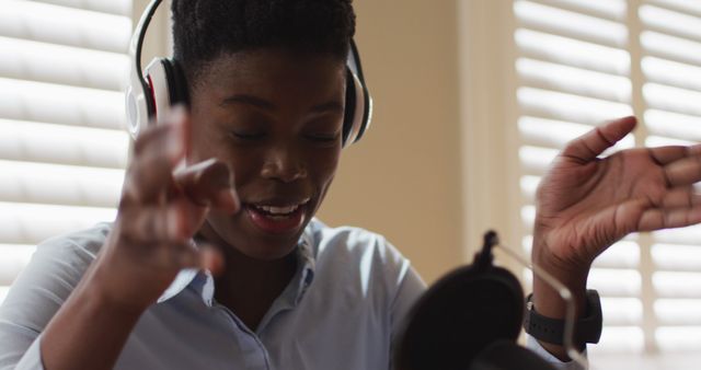 Person with afro hairstyle wearing headphones and gesturing expressively while recording podcast. Suitable for use in articles about podcasting, audio production, expressive communication, remote work, or content creation.