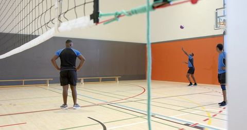 African american men practicing volleyball serve on indoor gym court for team training