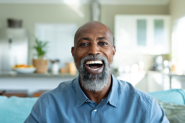 Senior African American man smiling warmly in a bright living room. Ideal for use in advertisements, articles, or websites focusing on senior living, happiness, home life, or health and wellness. Perfect for illustrating themes of joy, relaxation, and quality time spent at home.