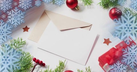 Blank holiday greeting card resting on kraft envelope with red baubles and evergreen