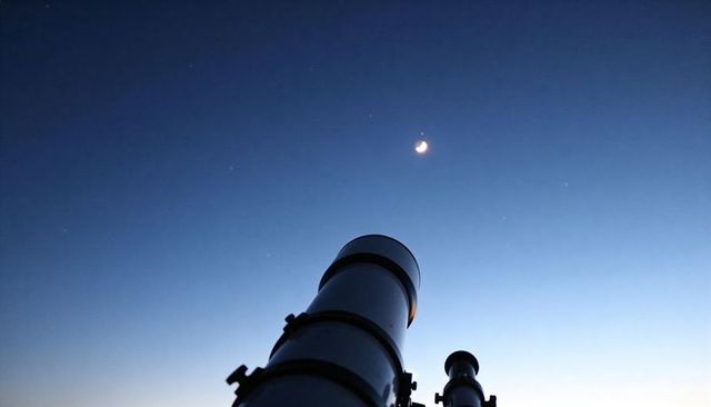 Telescope pointing at crescent moon and bright planet at twilight for stargazing and astronomy