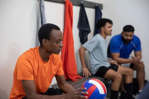 Diverse volleyball teammates sitting on bench holding ball preparing for practice or match