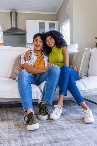 Smiling diverse couple cozy on sofa in modern open-plan living room wearing sneakers