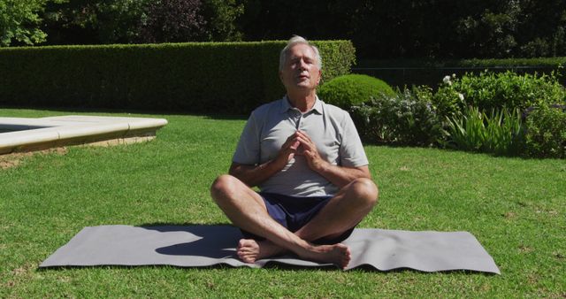 Caucasian senior man practicing yoga meditating in garden in the sun. at home in isolation during quarantine lockdown.