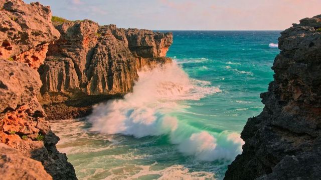 Turquoise waves crashing against jagged limestone cliffs at rocky cove at sunset
