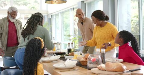 Multigenerational diverse family gathering around table sharing meal in sunlit dining room