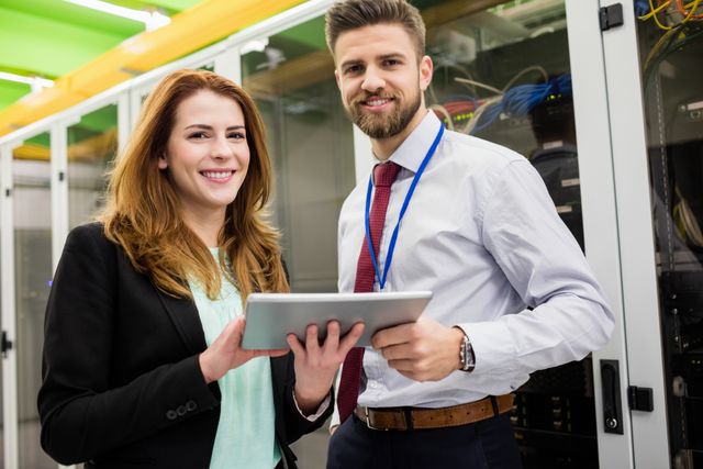 Portrait of smiling technicians standing in server room with digital tablet