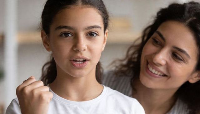 Young girl speaking confidently with clenched fist while mother smiling in supportive moment