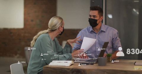 Masked colleagues collaborating with digital data overlay at desk