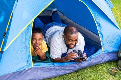 Father and son bonding in blue tent using binoculars for backyard camping and nature watching