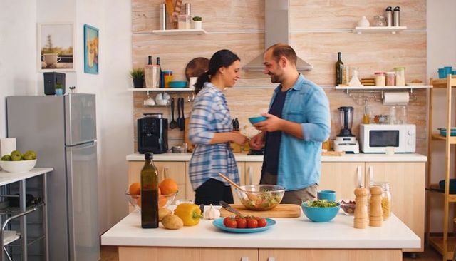 Couple preparing dinner together in modern kitchen exchanging blue bowl making salad