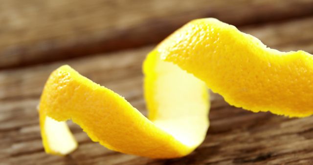 A vibrant twist of lemon peel rests on a wooden surface, its bright yellow color standing out - Download Free Stock Photos Pikwizard.com