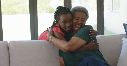 African grandmother hugging granddaughter on couch showing warm multigenerational bond at home