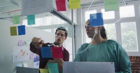 Diverse team brainstorming on glass wall at office meeting