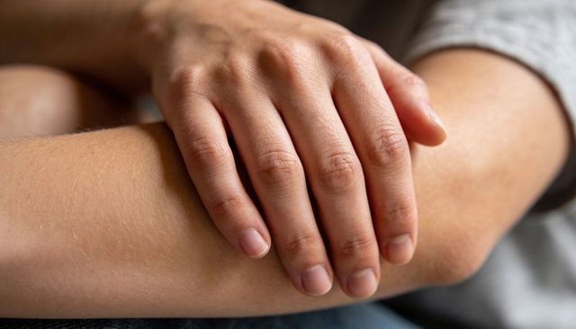 Resting hands with relaxed fingers on lap showing skin texture, knuckles and forearm detail