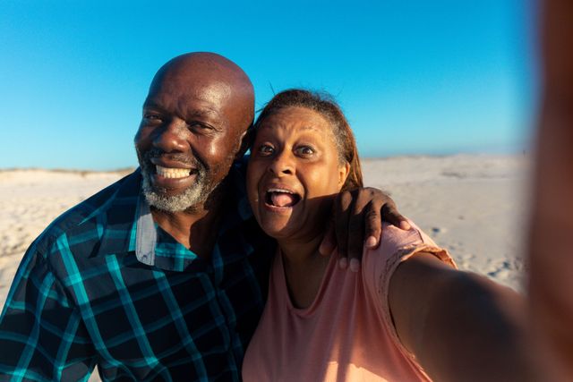 Senior African American couple enjoying a sunny day at the beach, taking a selfie and smiling. Perfect for use in advertisements, travel brochures, retirement planning materials, and lifestyle blogs promoting happiness, love, and active living in older age.