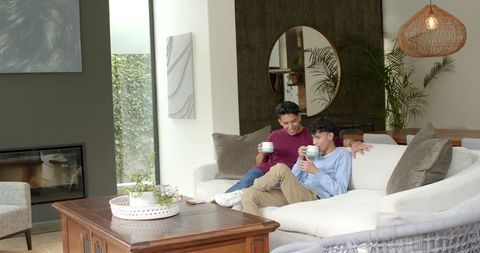 Two Men Relaxing on Sofa Holding Mugs in Cozy Living Room