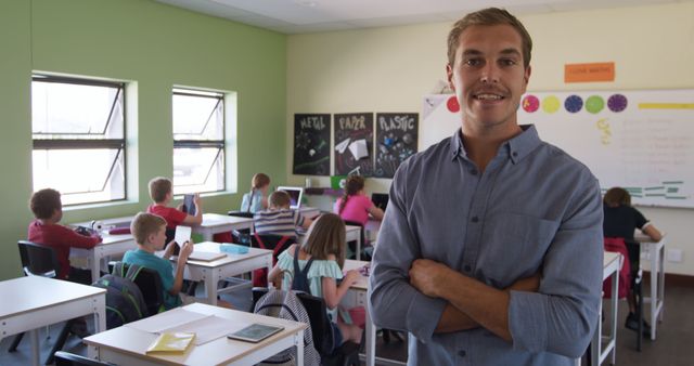 Confident teacher standing in classroom with young students studying at their desks. Ideal for educational materials, school brochures, teacher recruitment, and promoting academic programs.