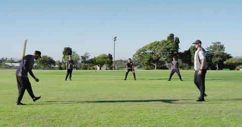 Amateur cricket team practicing on sunny park field with batter swinging wooden bat