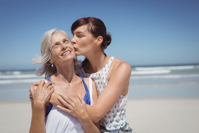 Young woman kissing her mother at beach during sunny day