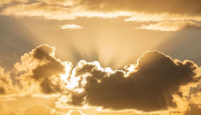 Golden Crepuscular Rays Breaking Through Dark Cumulus Clouds Over Warm Dawn Horizon