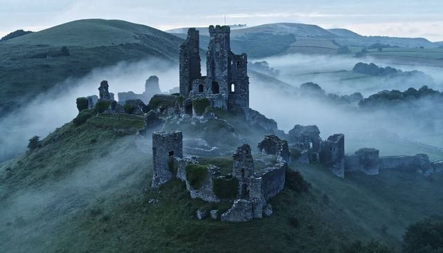 Misty medieval castle ruins crowning lush hill with winding fog-filled valleys