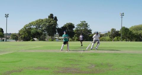 Two batsmen running single on sunny cricket field with umpire and stumps